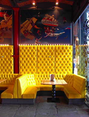 Yellow upholstered booth seating with circus themed wall graphics above in a Liverpool cafe bar interior