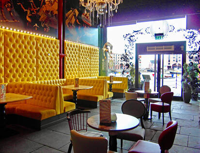 Looking across to the huge glazed facade near the yellow upholstered seating at this cafe bar interior in Liverpool