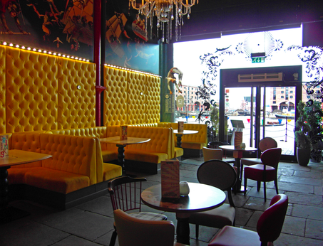 Yellow booth seating with graphics on the wall above in this cafe bar in Liverpool with a large glazed facade