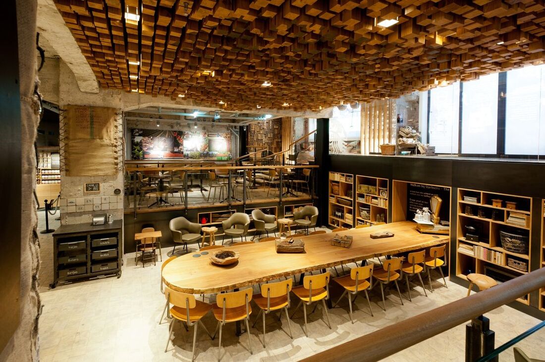 Large communal table and seating area with artistic ceiling installation in this neutral coloured Starbucks cafe interior in Amsterdam
